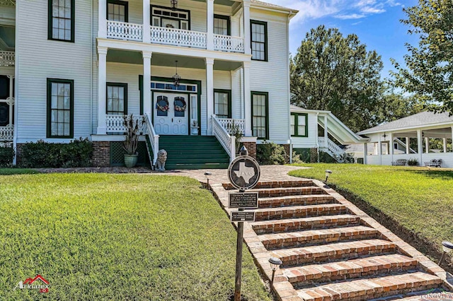 entrance to property with a yard, a balcony, covered porch, and french doors