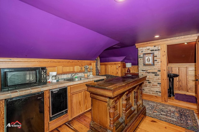 bar featuring tile countertops, light hardwood / wood-style floors, sink, and wooden walls