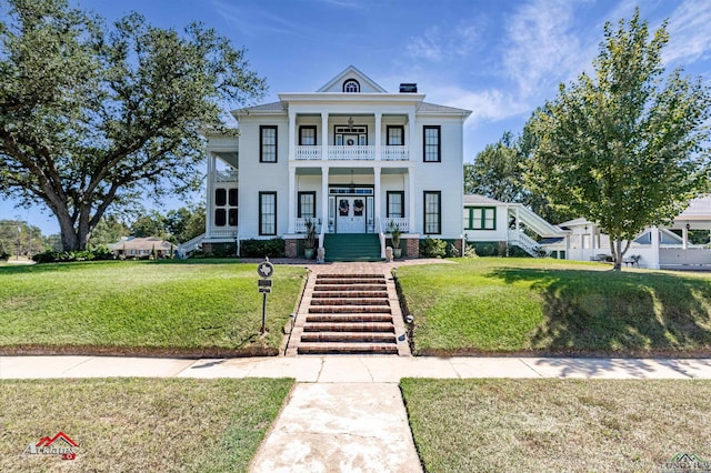 neoclassical home with a porch, a balcony, and a front lawn