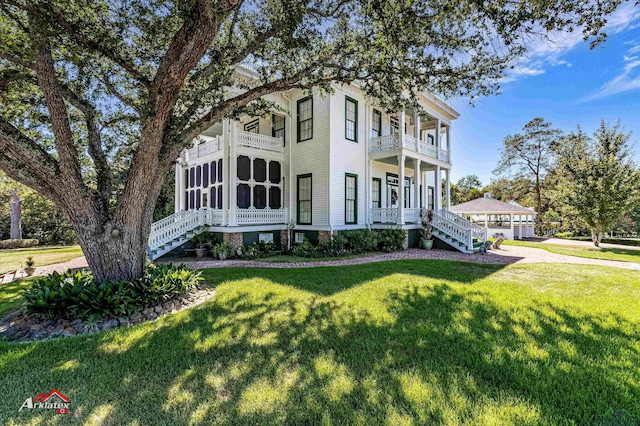 victorian-style house featuring a balcony, a front lawn, and a sunroom