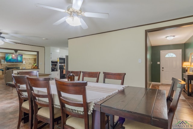 dining area featuring ceiling fan, tile patterned flooring, and a brick fireplace