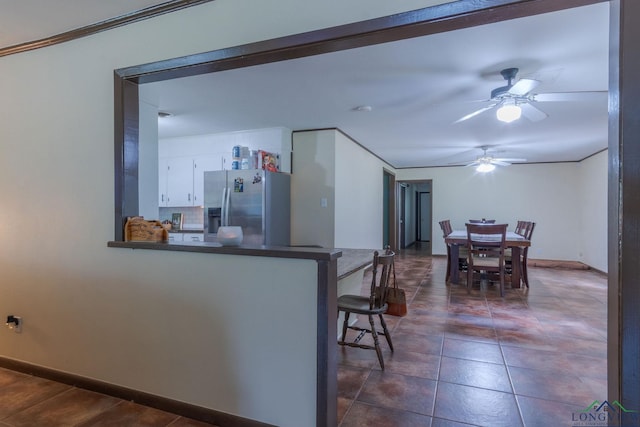 kitchen featuring kitchen peninsula, a kitchen breakfast bar, ornamental molding, stainless steel fridge with ice dispenser, and white cabinetry