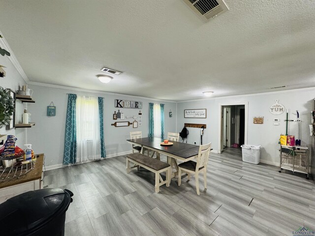 dining space featuring light wood-type flooring, a textured ceiling, and ornamental molding