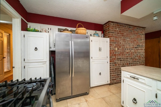 kitchen featuring a textured ceiling, white cabinetry, stainless steel appliances, brick wall, and light countertops