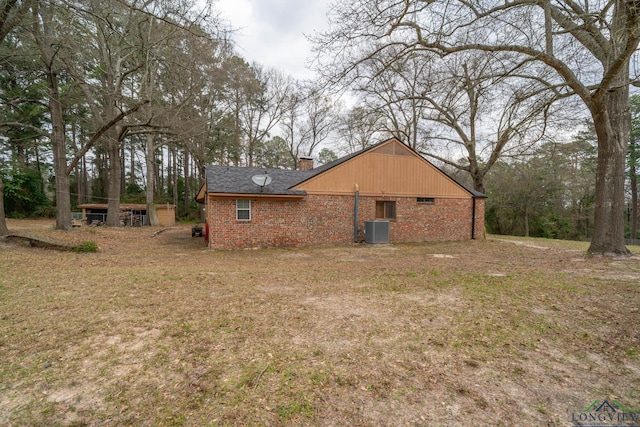 back of house featuring central air condition unit, a lawn, brick siding, and a chimney