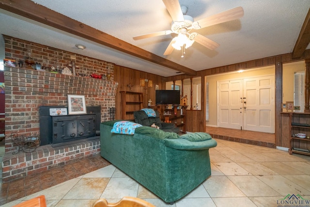 tiled living room with beam ceiling, wood walls, a textured ceiling, and a wood stove