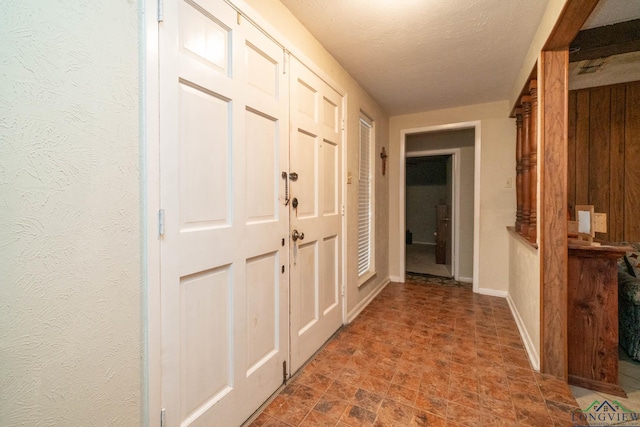 hall with baseboards, a textured ceiling, and a textured wall