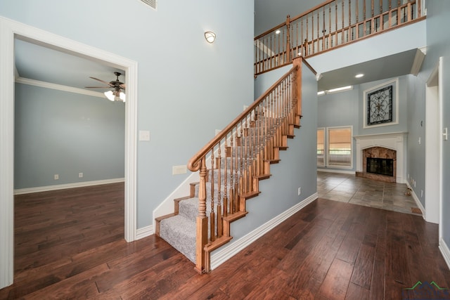 stairway with ceiling fan, a towering ceiling, wood-type flooring, and ornamental molding