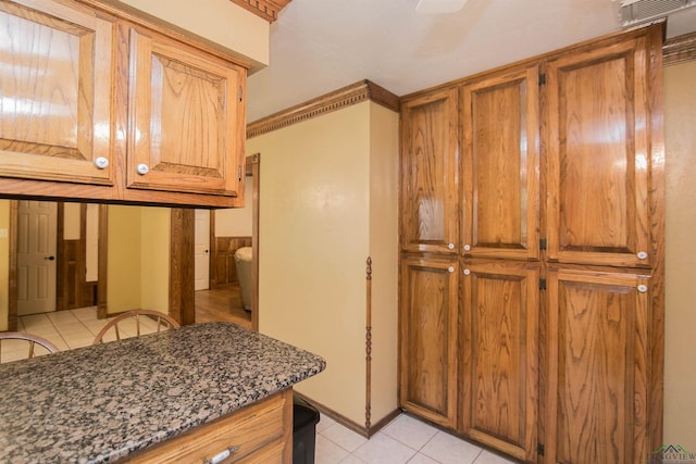 kitchen with dark stone countertops, light tile patterned floors, and ornamental molding