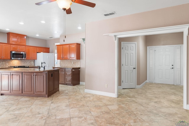 kitchen with sink, ceiling fan, white refrigerator, a center island with sink, and decorative backsplash