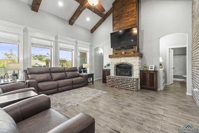 living room featuring beamed ceiling, ceiling fan, a stone fireplace, and a high ceiling