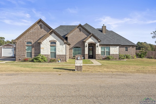 french country inspired facade featuring a front lawn, an outdoor structure, and a garage