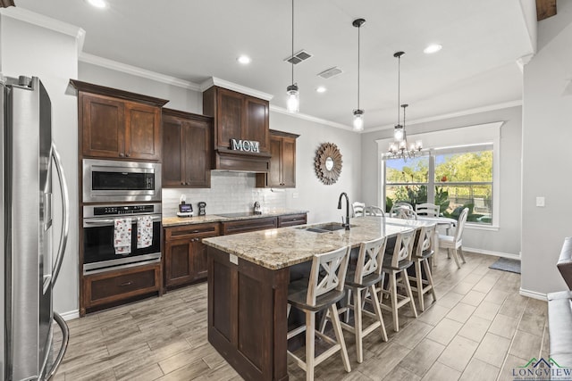 kitchen featuring light stone countertops, sink, stainless steel appliances, decorative light fixtures, and a kitchen island with sink