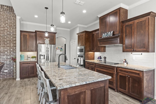 kitchen featuring light stone countertops, appliances with stainless steel finishes, light wood-type flooring, sink, and a center island with sink