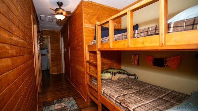 bedroom with dark hardwood / wood-style flooring, ceiling fan, wooden walls, and brick wall