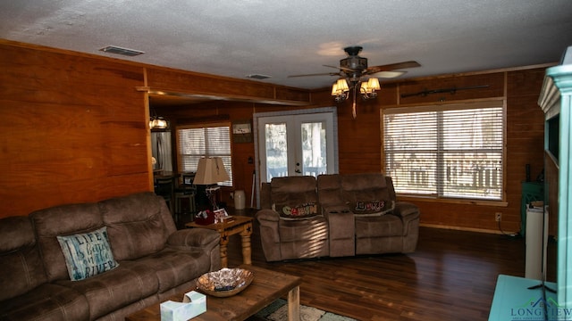 living room featuring french doors, dark hardwood / wood-style flooring, ceiling fan with notable chandelier, a textured ceiling, and wooden walls