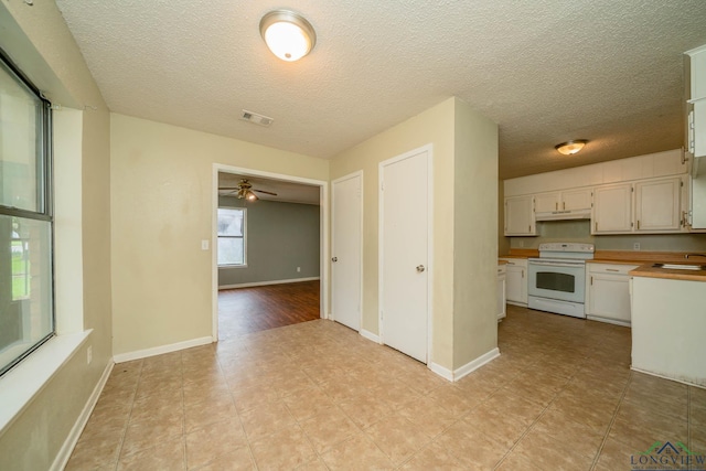 308 N Lee Dr, Gladewater, TX 75647 - kitchen with white electric range oven, under cabinet range hood, ceiling fan, white cabinetry, and a textured ceiling