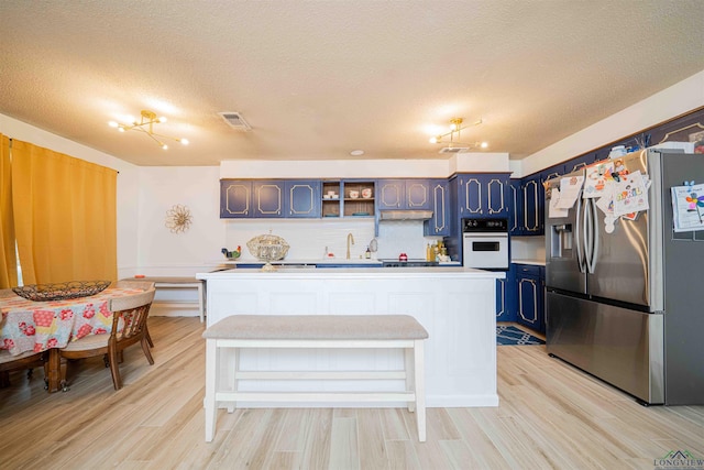 kitchen with a textured ceiling, white oven, visible vents, stainless steel refrigerator with ice dispenser, and light countertops
