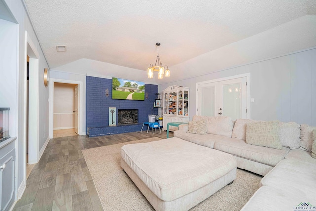 living area with wood finished floors, a textured ceiling, an inviting chandelier, lofted ceiling, and visible vents