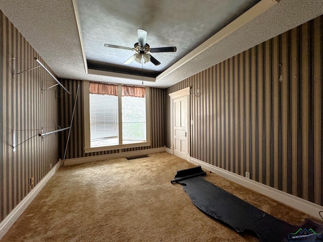 exercise room featuring ceiling fan, carpet flooring, a tray ceiling, and a textured ceiling