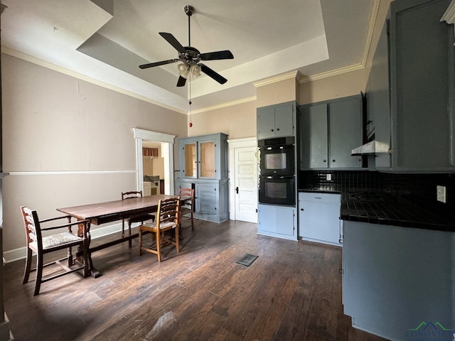 kitchen featuring dark hardwood / wood-style floors, backsplash, black double oven, tile counters, and a raised ceiling