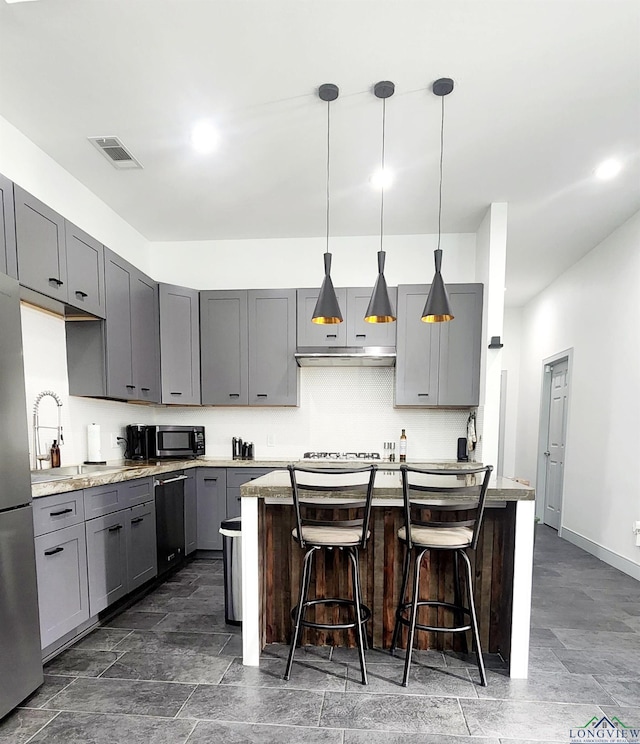 kitchen featuring gray cabinetry, a kitchen bar, hanging light fixtures, and stainless steel appliances