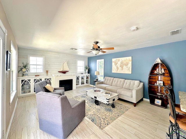 living room featuring light hardwood / wood-style flooring, a brick fireplace, and ceiling fan