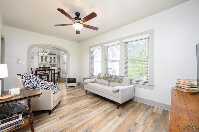 living room with heating unit, a healthy amount of sunlight, ceiling fan with notable chandelier, and light wood-type flooring