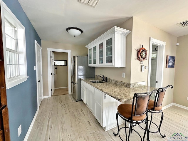 kitchen with white cabinets, light hardwood / wood-style floors, light stone countertops, and sink