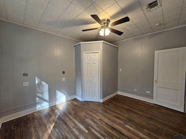 empty room with dark hardwood / wood-style flooring, wooden walls, ceiling fan, and crown molding