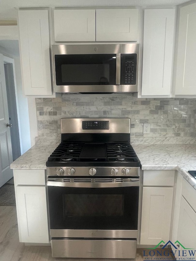 kitchen featuring white cabinets, backsplash, light stone counters, stainless steel appliances, and light wood-type flooring