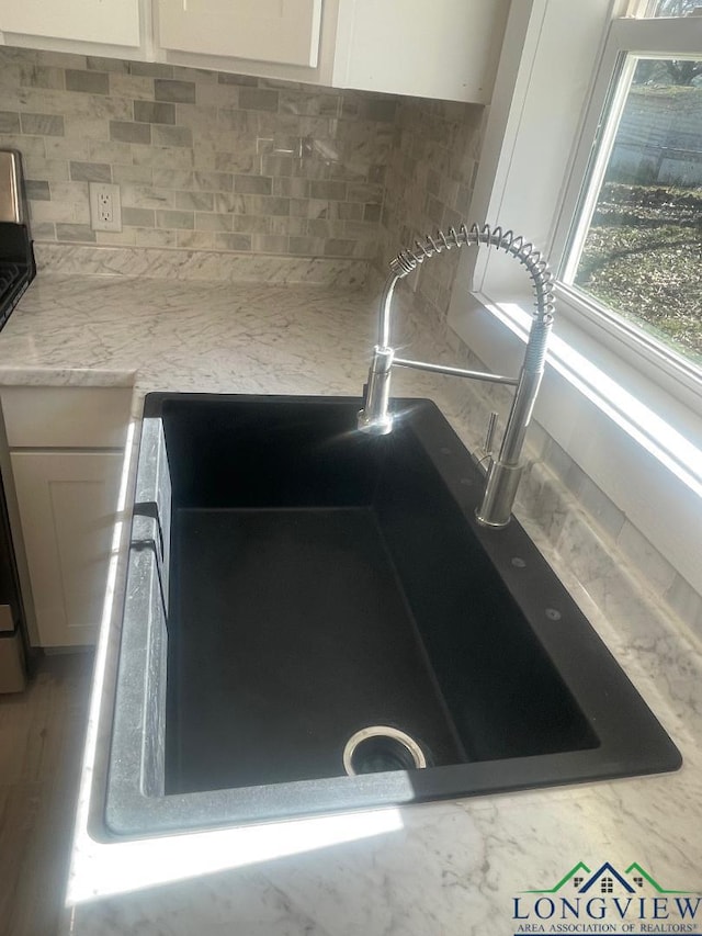 room details featuring sink, decorative backsplash, and white cabinets