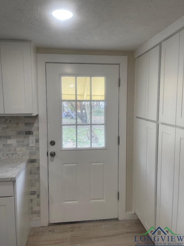 doorway to outside with light hardwood / wood-style flooring and a textured ceiling