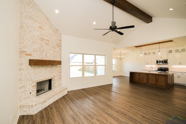 unfurnished living room featuring beam ceiling, dark wood-type flooring, a stone fireplace, high vaulted ceiling, and ceiling fan with notable chandelier