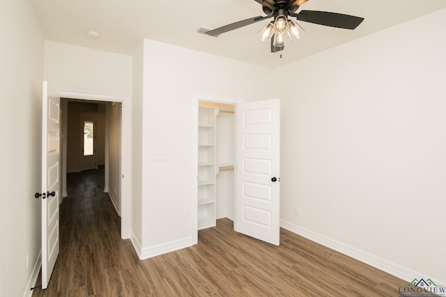 unfurnished bedroom with a closet, a spacious closet, ceiling fan, and dark wood-type flooring