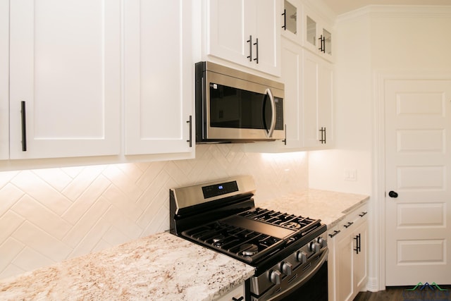 kitchen with backsplash, stainless steel appliances, white cabinetry, and light stone counters