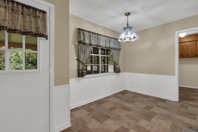 unfurnished dining area with a chandelier and a textured ceiling