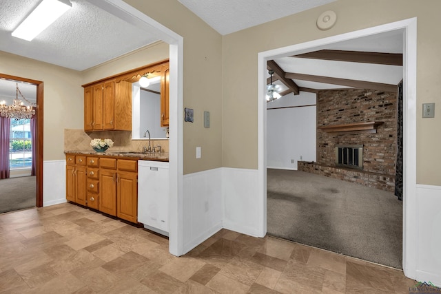 kitchen with white dishwasher, lofted ceiling with beams, sink, a brick fireplace, and a textured ceiling