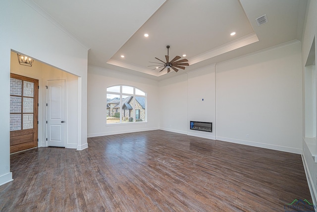 unfurnished living room featuring a tray ceiling, dark wood-type flooring, ornamental molding, and ceiling fan with notable chandelier