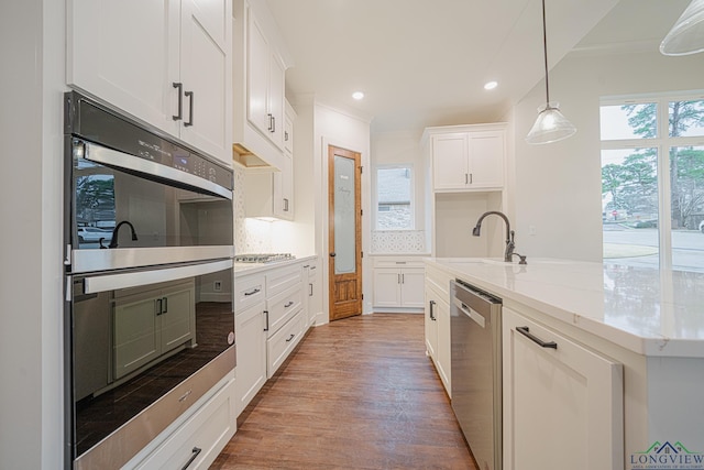 kitchen with decorative light fixtures, a wealth of natural light, stainless steel appliances, light stone countertops, and white cabinets