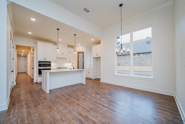 kitchen with white cabinetry, ornamental molding, an island with sink, and hardwood / wood-style flooring