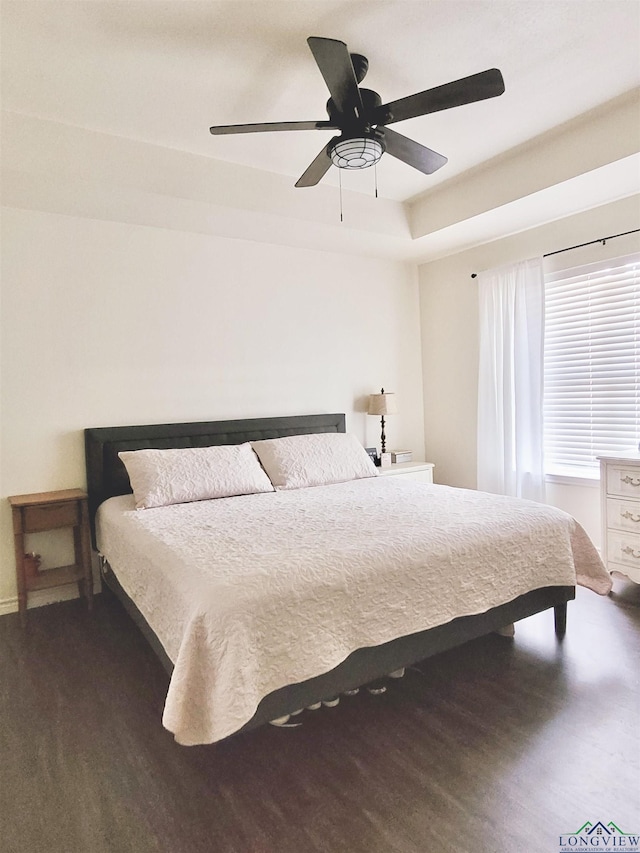 bedroom featuring a raised ceiling, ceiling fan, and dark hardwood / wood-style flooring