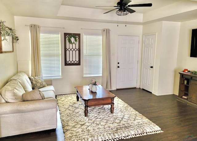 living room with dark hardwood / wood-style flooring, a tray ceiling, and ceiling fan