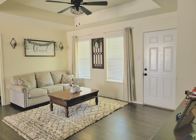 living room with dark hardwood / wood-style flooring, a raised ceiling, and ceiling fan