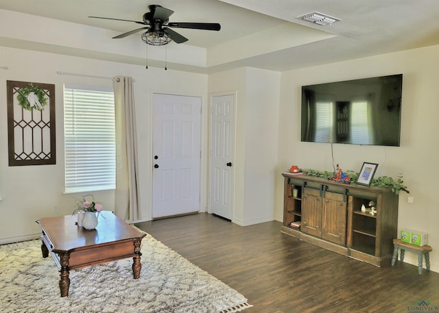 living room with dark hardwood / wood-style flooring, ceiling fan, and a raised ceiling