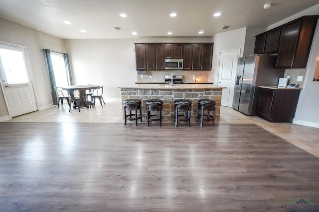 1126 Ruddy Duck, New Braunfels, TX 78130 - kitchen with stainless steel appliances, a center island with sink, backsplash, dark brown cabinets, and a kitchen breakfast bar