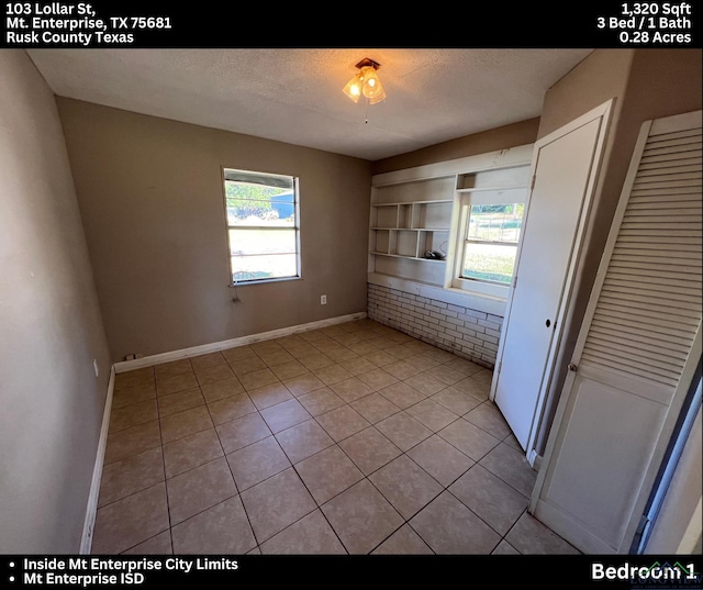 interior space featuring a textured ceiling, light tile patterned flooring, and built in shelves