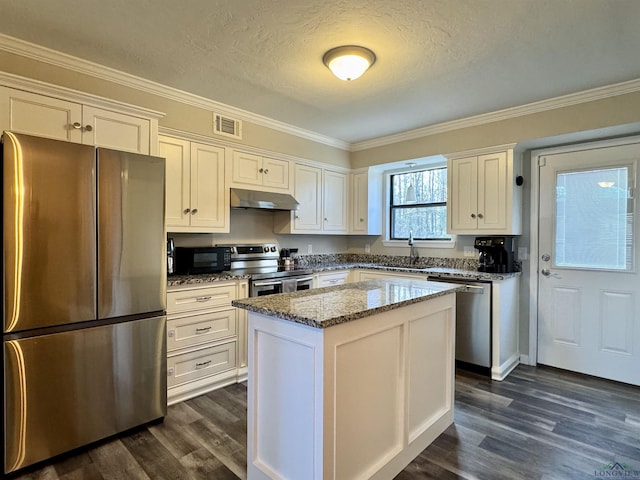 kitchen featuring a textured ceiling, white cabinets, appliances with stainless steel finishes, a kitchen island, and stone countertops