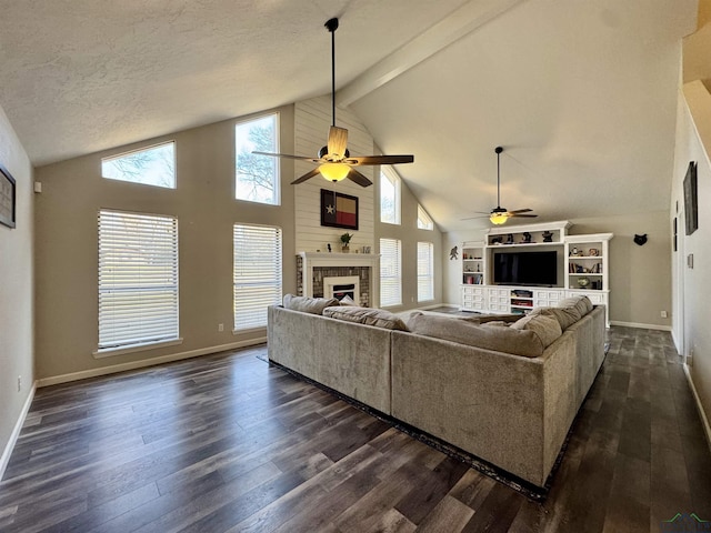 living room featuring a textured ceiling, dark hardwood / wood-style flooring, ceiling fan, a brick fireplace, and beam ceiling