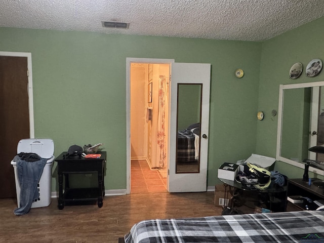 bedroom featuring visible vents, a textured ceiling, baseboards, and wood finished floors